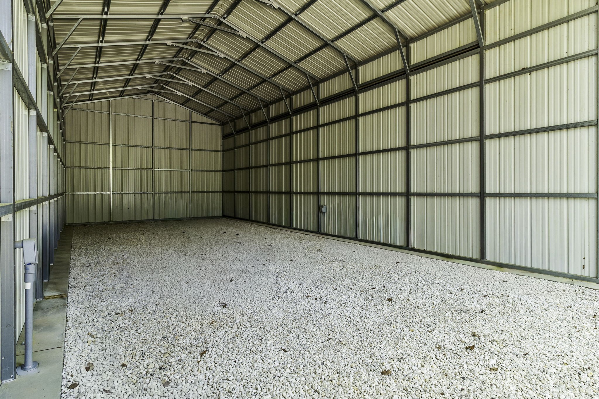 21 Red Oak Circle Point Blank, TX 77364 - Photo 28 of 32 This photo shows a spacious metal storage building with a high ceiling and a gravel floor, ideal for storing your RV, extra vehicles or equipment.