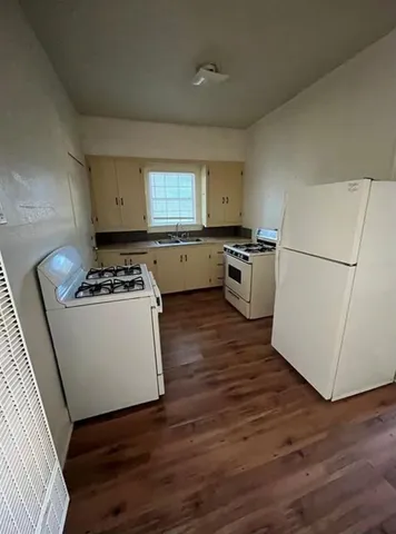 a kitchen with a refrigerator a stove a wooden floor and white cabinets