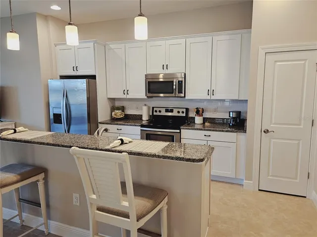 a kitchen with stainless steel appliances granite countertop a sink a stove a refrigerator and white cabinets
