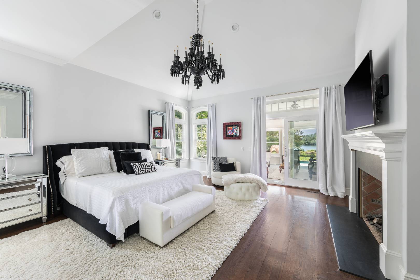 19 Kellis Way Bridgehampton, NY 11932 - Photo 14 of 26 a bedroom with a large bed flat screen tv and a fireplace