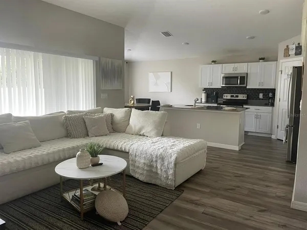 a living room with stainless steel appliances furniture and a kitchen view