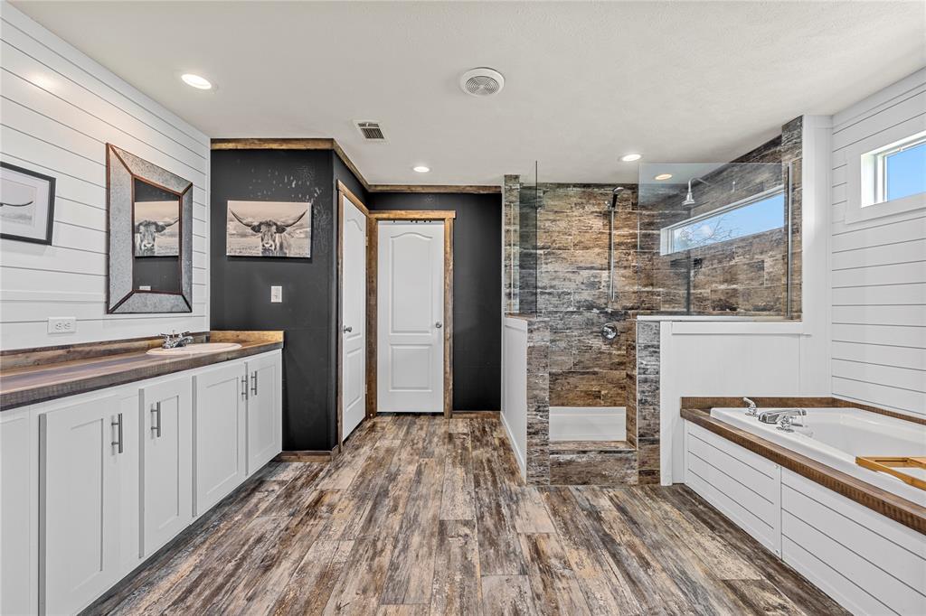 602 3rd Street Abbott, TX 76621 - Photo 21 of 40 Bathroom featuring wood-finish flooring, a freestanding soaking tub, a walk-in shower with glass enclosure, a vanity with a countertop, and horizontal paneling