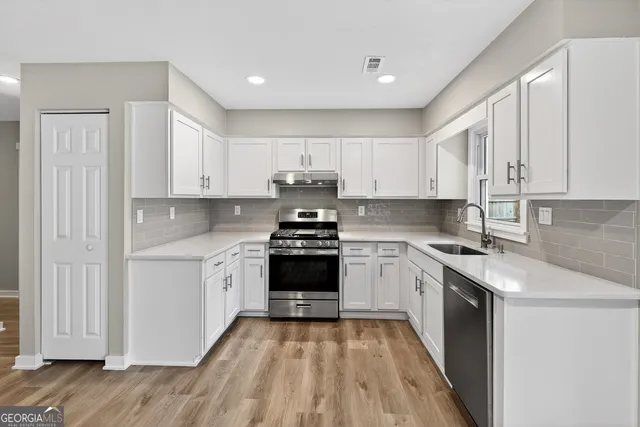 a kitchen with stainless steel appliances granite countertop a stove a sink and white cabinets