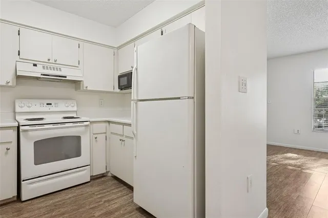 a white refrigerator freezer and a stove sitting inside of a kitchen with granite countertop white cabinets and wooden floor