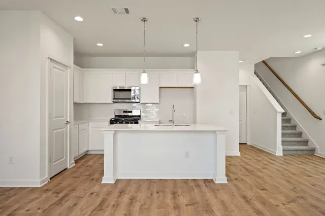 a kitchen with stainless steel appliances granite countertop a refrigerator a sink dishwasher a stove and white cabinets with wooden floor