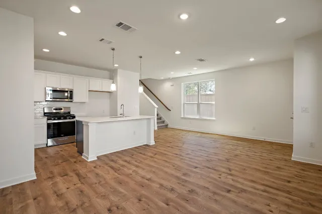 a large kitchen with stainless steel appliances a large counter top and wooden floors