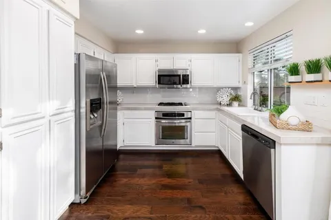 a kitchen with stainless steel appliances granite countertop a refrigerator a sink a stove top oven and wooden floor