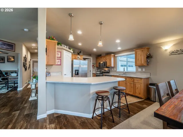 a kitchen with stainless steel appliances kitchen island granite countertop a dining table chairs and a refrigerator