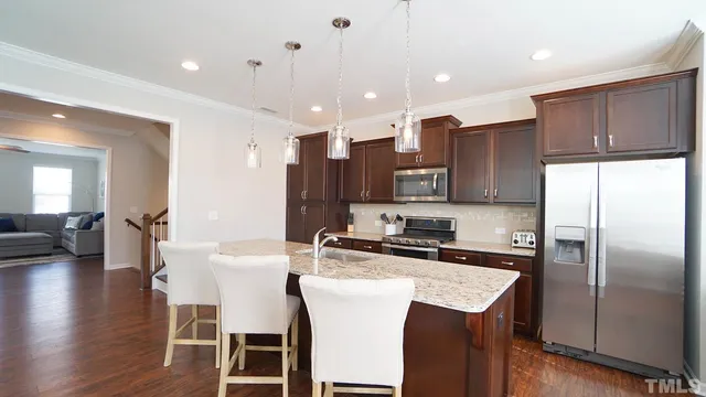 a kitchen with stainless steel appliances granite countertop a refrigerator a stove a sink a dining table and chairs with wooden floor