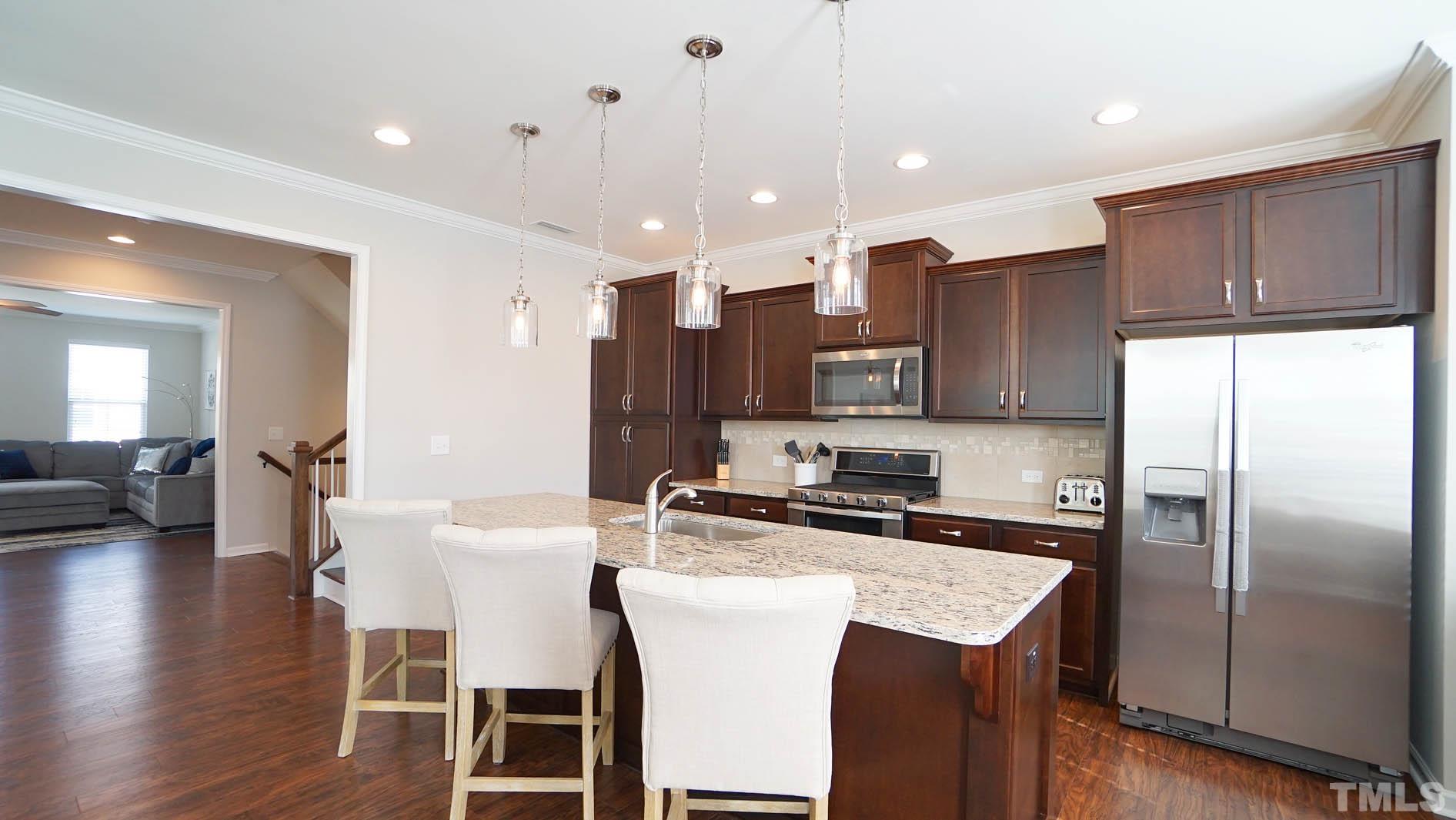 540 Metro Station Apex, NC 27502 - Photo 18 of 45 a kitchen with stainless steel appliances granite countertop a refrigerator a stove a sink a dining table and chairs with wooden floor