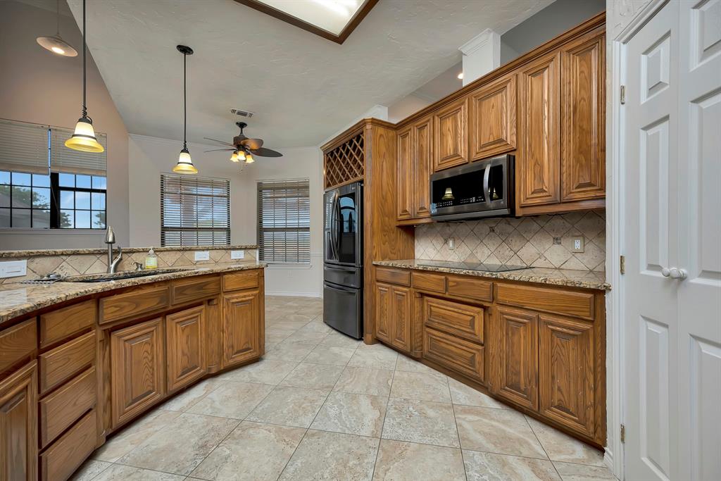 5520 White Settlement Road Weatherford, TX 76087 - Photo 13 of 39 Kitchen featuring stainless steel microwave, smart refrigerator, brown cabinetry, backsplash, and a ceiling fan