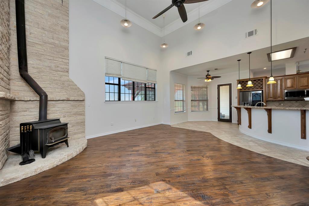 5520 White Settlement Road Weatherford, TX 76087 - Photo 18 of 39 Unfurnished living room featuring a ceiling fan, a wood stove, wood finished floors, a high ceiling, and crown molding