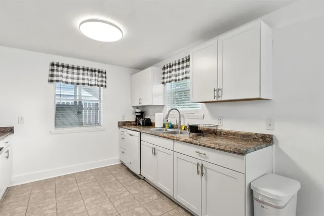 a kitchen with granite countertop white cabinets white appliances a sink and a window