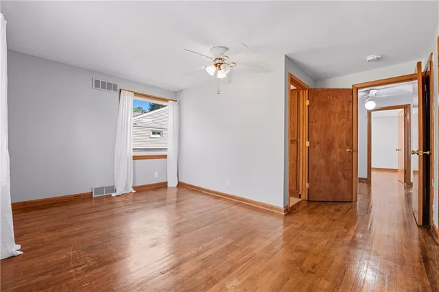 an empty room with wooden floor chandelier fan and windows