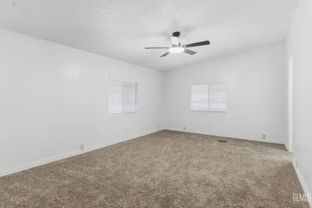 an empty room with chandelier fan and windows