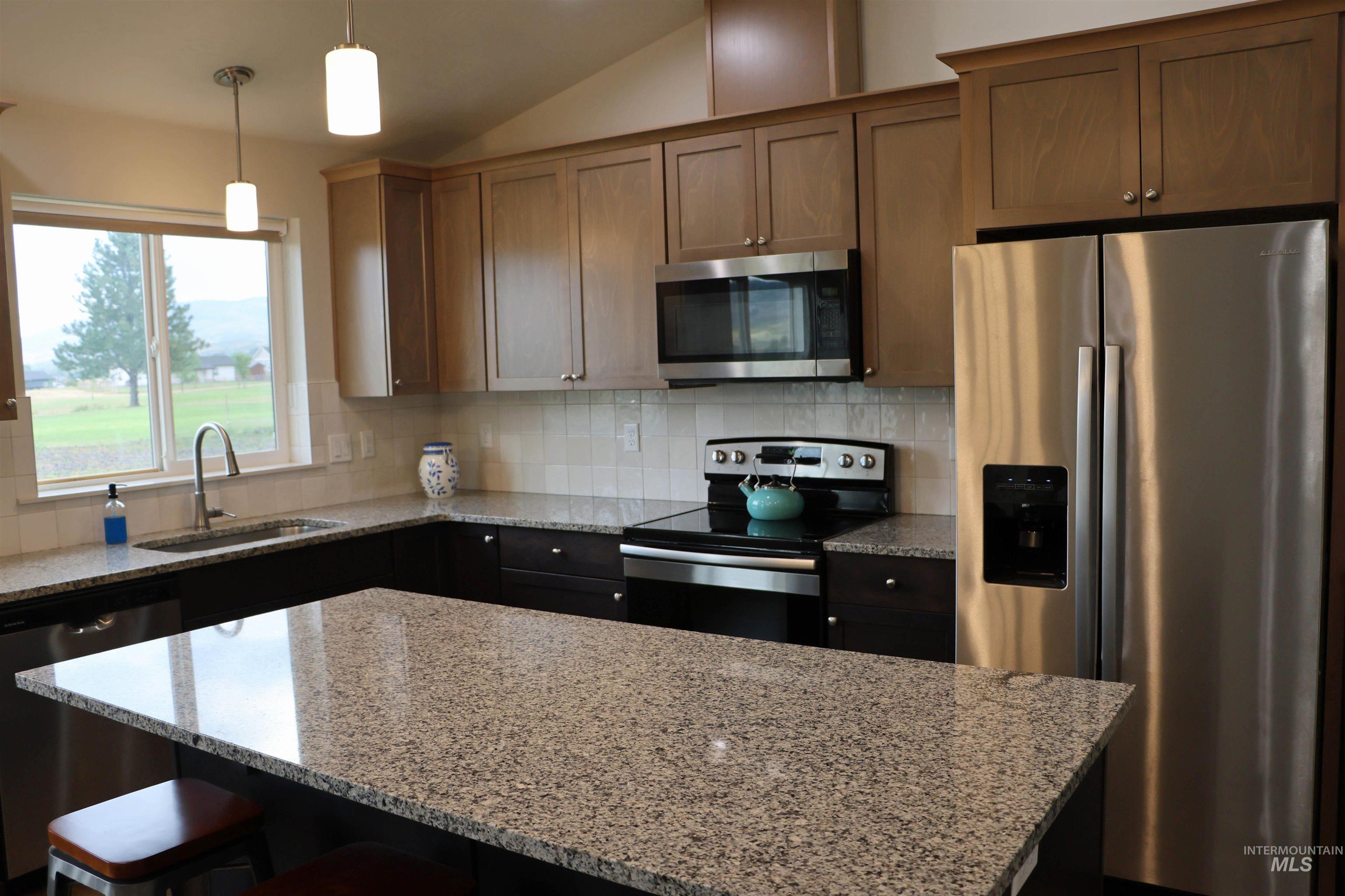 2272 Golf Lane Council, ID 83612 - Photo 8 of 32 Kitchen featuring stainless steel appliances, lofted ceiling, light stone counters, a kitchen island, and a kitchen bar