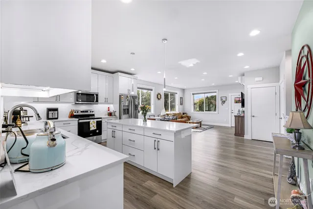 a kitchen with stainless steel appliances kitchen island granite countertop a stove top oven a sink dishwasher and a refrigerator with wooden floor