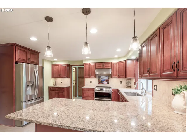 a kitchen with stainless steel appliances kitchen island granite countertop a refrigerator oven a sink a stove a dining table and chairs with wooden floor