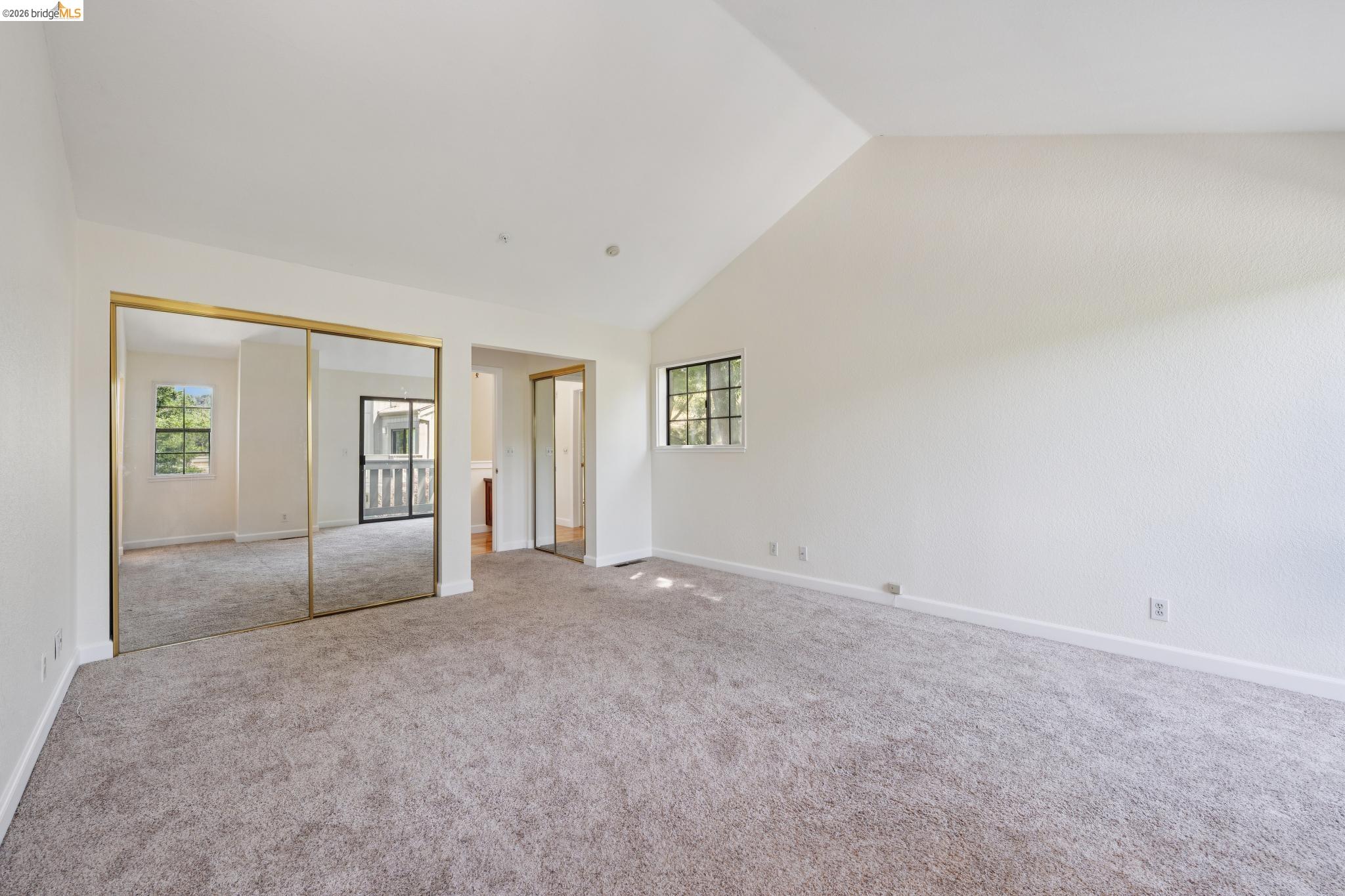 261 Redhawk Road Novato, CA 94949 - Photo 30 of 44 Spacious room featuring vaulted ceilings, neutral-toned carpeting, mirrored closet doors with gold-tone frames, and multiple windows providing natural illumination