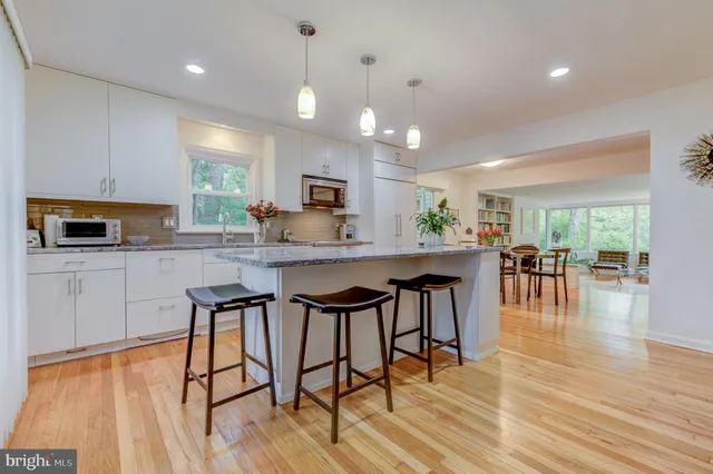 a kitchen with stainless steel appliances kitchen island granite countertop a stove a refrigerator a sink a dining table and chairs with wooden floor