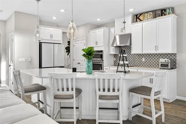 a kitchen with stainless steel appliances kitchen island granite countertop a refrigerator a stove a sink a dining table and chairs with wooden floor