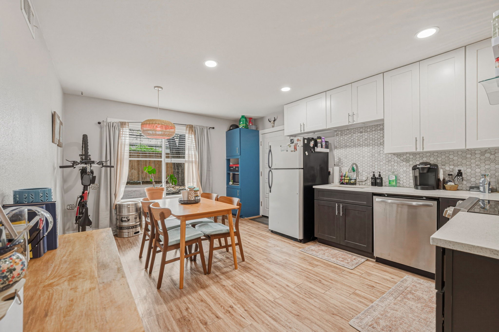 5332 Balcones Drive, Unit B Austin, TX 78731 - Photo 6 of 15 Kitchen and dining area featuring light wood tone flooring, white upper cabinetry, dark lower cabinetry, and a patterned tile backsplash