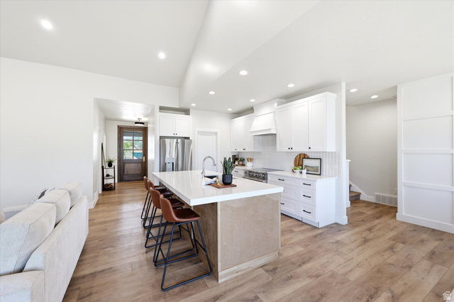 White kitchen cabinetry with black hardware, stainless steel appliances, and a central island with countertop seating