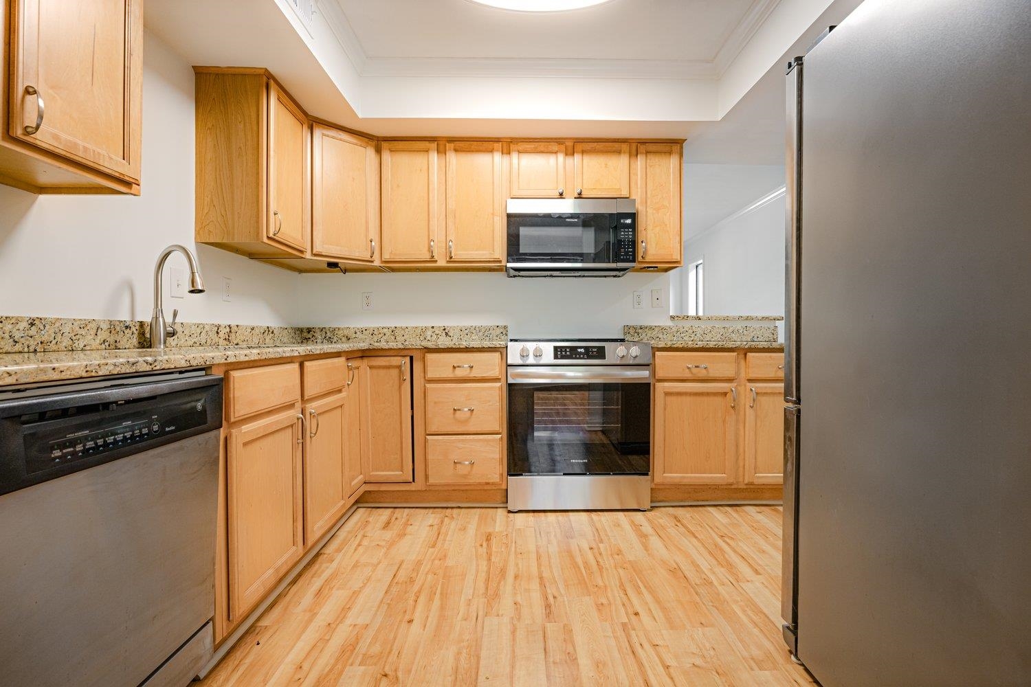 1847 Gray Ridge Cove, Unit 2 Germantown, TN 38138 - Photo 7 of 26 Kitchen with appliances with stainless steel finishes, a tray ceiling, light wood-style flooring, light brown cabinetry, and ornamental molding