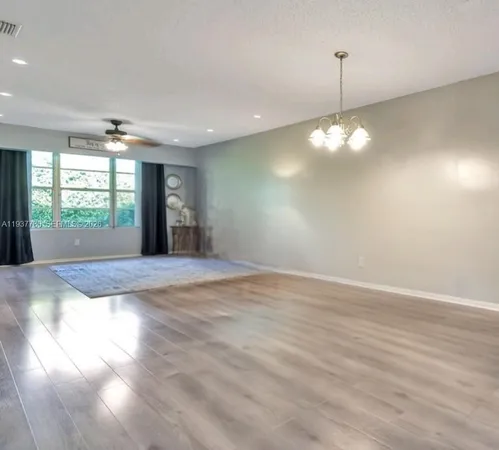 a view of an empty room with window and chandelier fan
