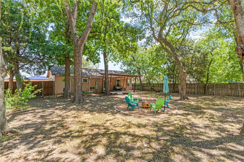 649 Peavy Road Dallas, TX 75218 - Photo 22 of 30 Spacious backyard with mature shade trees, a privacy fence, and a designated fire pit area