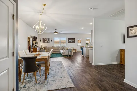 a view of a dining room and livingroom with furniture wooden floor a rug a flat screen tv a painting and a chandelier