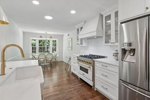 a kitchen with stainless steel appliances granite countertop a stove a sink dishwasher a refrigerator and a dining table with wooden floor