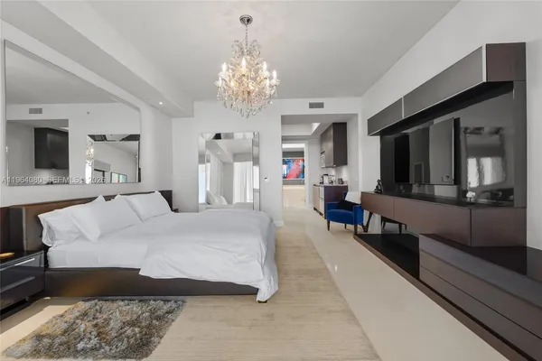 a spacious bedroom with a large bed a chandelier and dresser