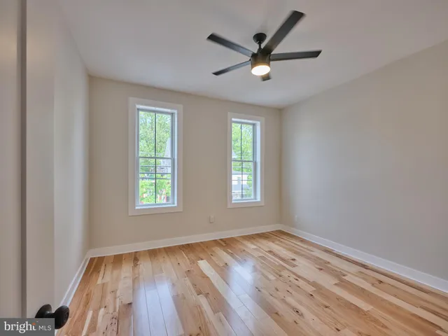 an empty room with wooden floor windows and fan