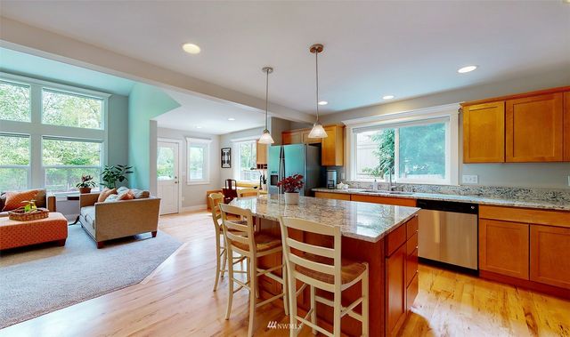 an open kitchen with granite countertop a stove a sink a dining table and chairs with wooden floor