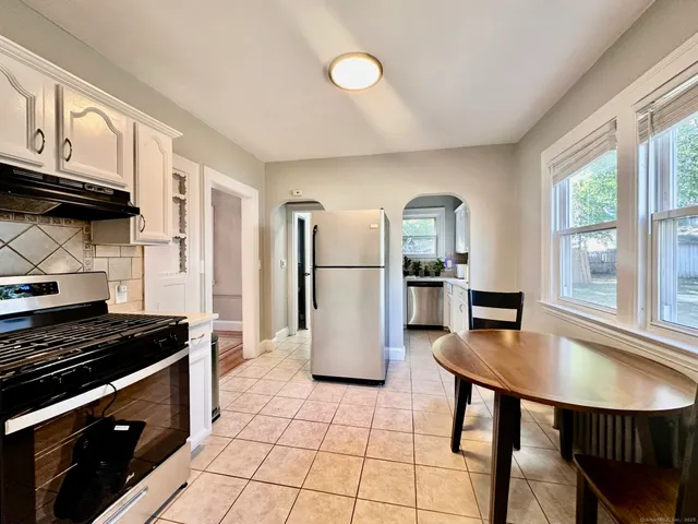 a kitchen with stainless steel appliances granite countertop a stove a refrigerator a sink a dining table and chairs