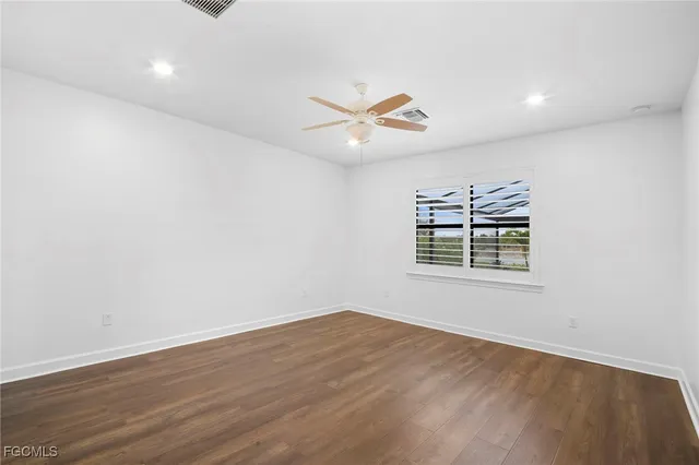 an empty room with wooden floor ceiling fan and windows