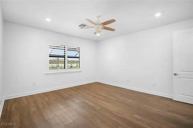 an empty room with wooden floor ceiling fan and windows