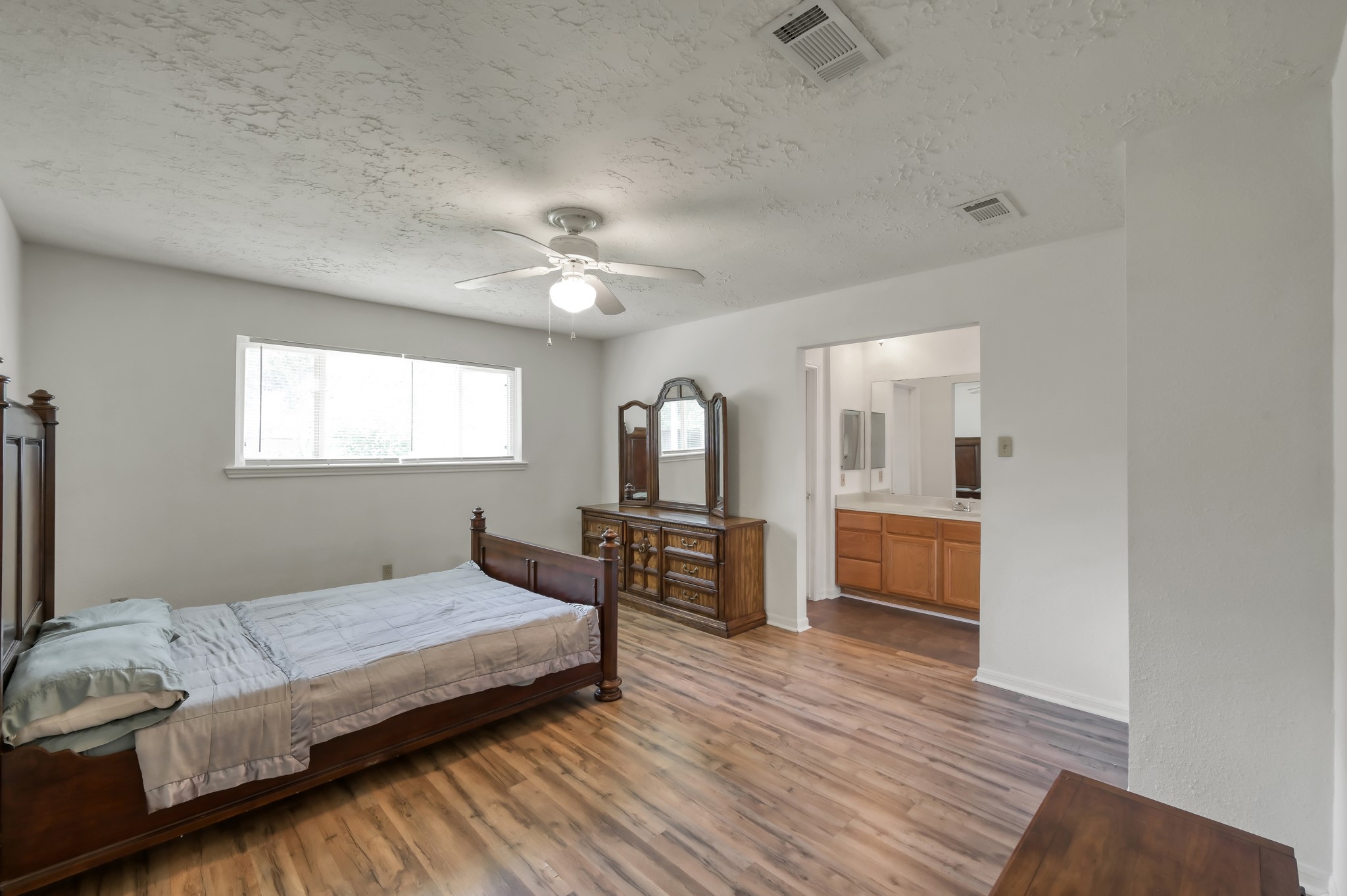 4314 Enchantedgate Drive Spring, TX 77373 - Photo 21 of 47 Spacious primary bedroom features wood flooring, a ceiling fan, and ample natural light from a large window. It includes an en-suite bathroom with a vanity, adding convenience and comfort.