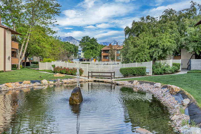 6852 Countrywoods Circle, Unit 5D Midvale, UT 84047 - Photo 46 of 50 Serene pond with a central rock fountain, bordered by decorative rockwork and manicured lawn