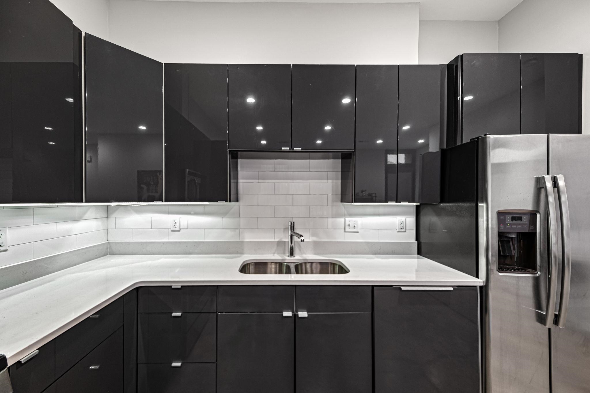 448 Tennessee Street Memphis, TN 38103 - Photo 31 of 39 Modern kitchen featuring dark glossy cabinetry, light countertops, subway tile backsplash, and a stainless steel double-door refrigerator