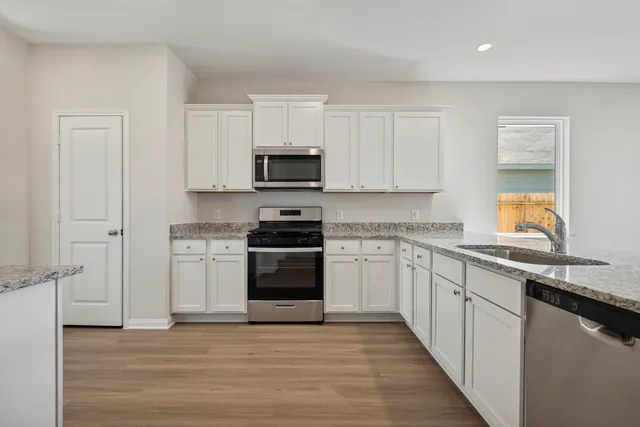 a kitchen with stainless steel appliances a stove top oven a sink a refrigerator white cabinets and a wooden floor