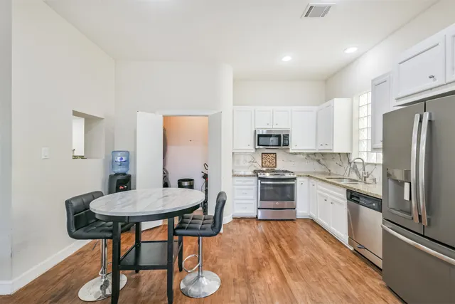 a kitchen with stainless steel appliances a stove a sink a refrigerator dining table and chairs