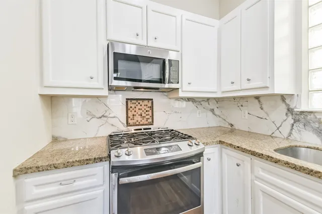 a kitchen with granite countertop white cabinets and a stove top oven