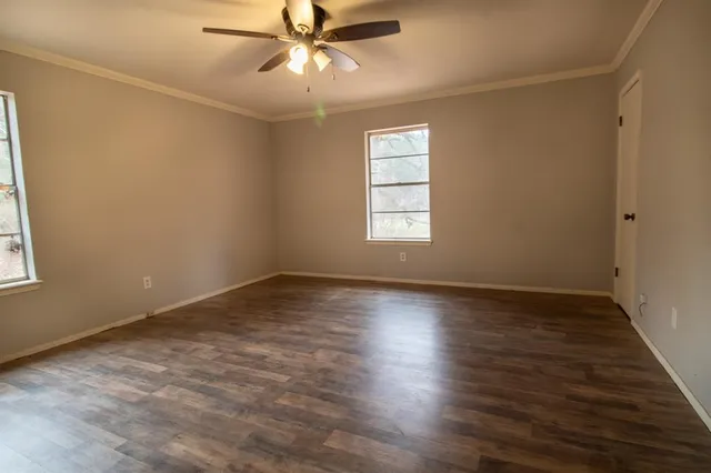 an empty room with wooden floor fan and windows