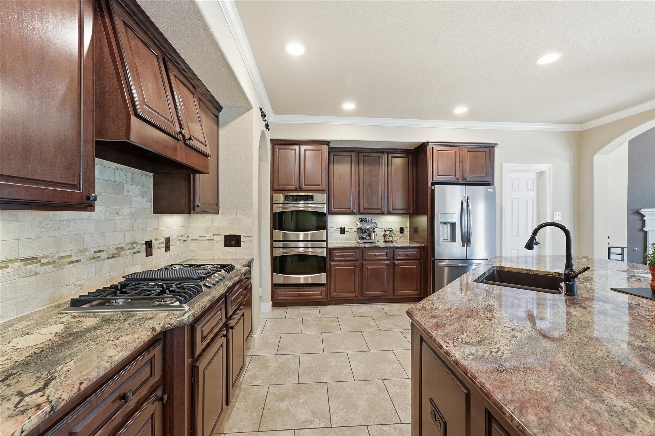 17710 Rough River Court Humble, TX 77346 - Photo 8 of 38 This spacious kitchen features elegant dark wood cabinetry, a sleek stainless appliances, and double ovens. The large island with a sink offers extra counter space, perfect for meal prep. Tiled flooring and a neutral backsplash complete the sophisticated look.