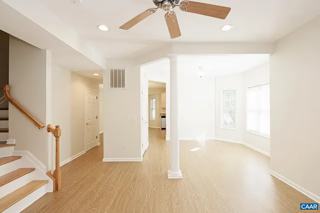 a view of an empty room with wooden floor and a ceiling fan