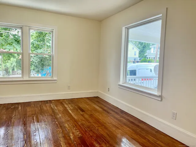 a view of an empty room with wooden floor and a window