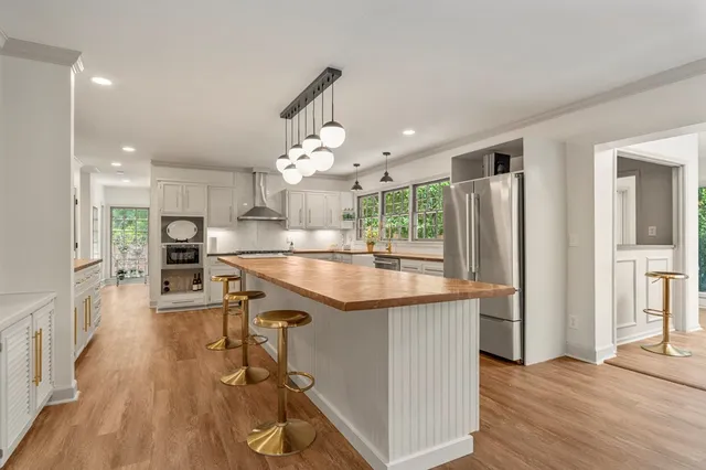 a kitchen with stainless steel appliances granite countertop a refrigerator a sink dishwasher a stove and a dining table with wooden floor