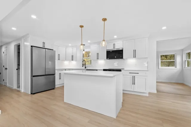 a kitchen with stainless steel appliances granite countertop a refrigerator a sink dishwasher a oven and white cabinets with wooden floor